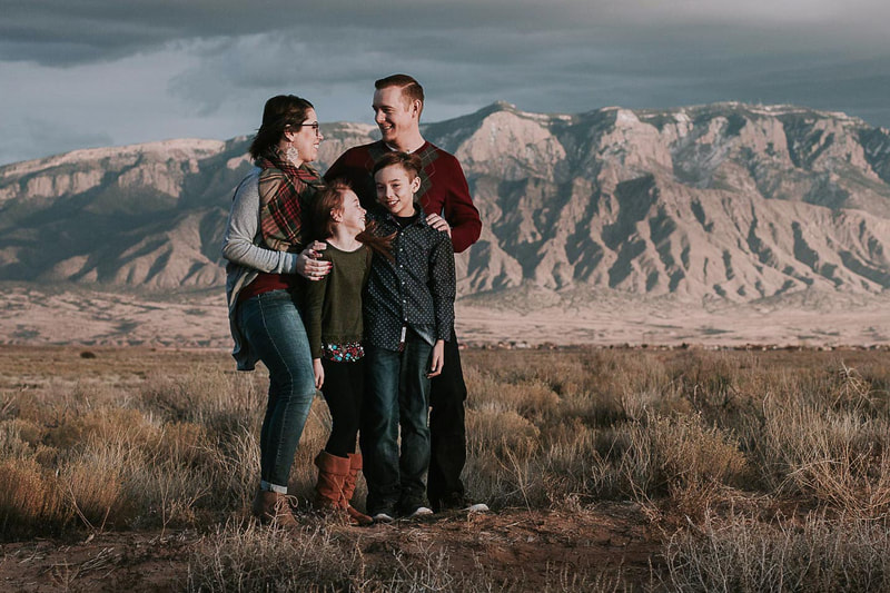 Family of 4 look at eachother in front of dramatic view of the mountains.