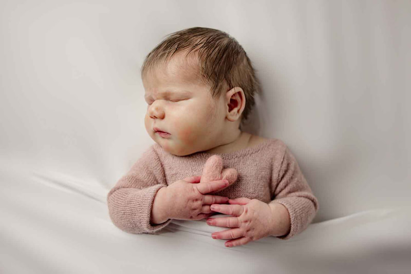 Sleeping baby on white blanket holding pink heart.