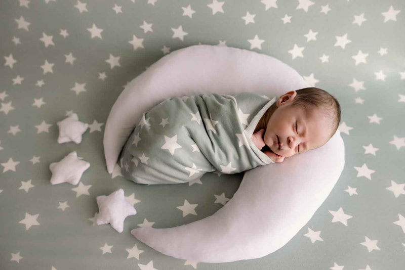 Sleeping newborn on white moon on light green blanket with white stars