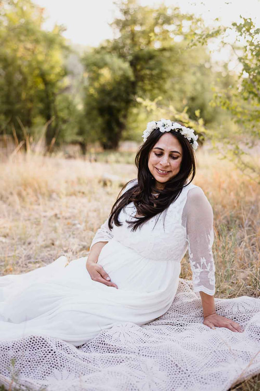 Mother to be in white dress and white flower crown sitting on the ground