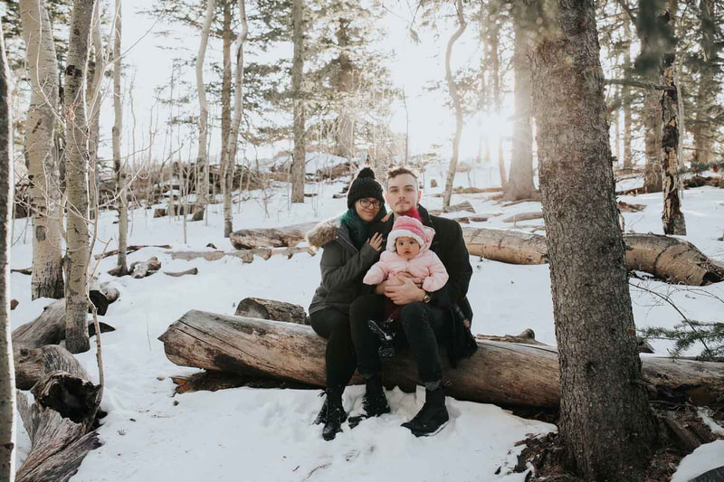 Couple holding baby sitting in the snow on a log.