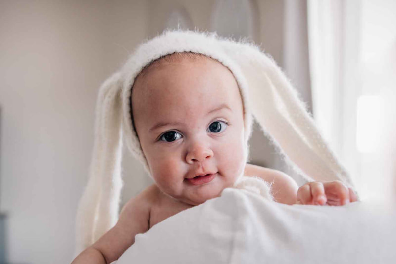 Young baby looks over shoulder while wearing white fuzzy rabbit hat.