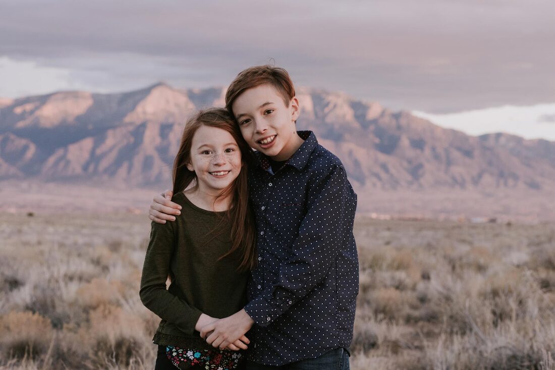 Smiling brother and sister in front of sunset and Sandia mountains 