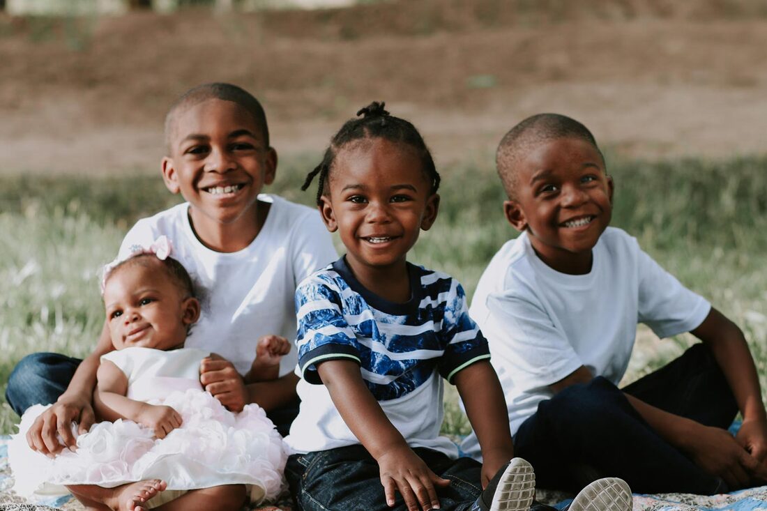 Several children smiling, older brother holding baby sister