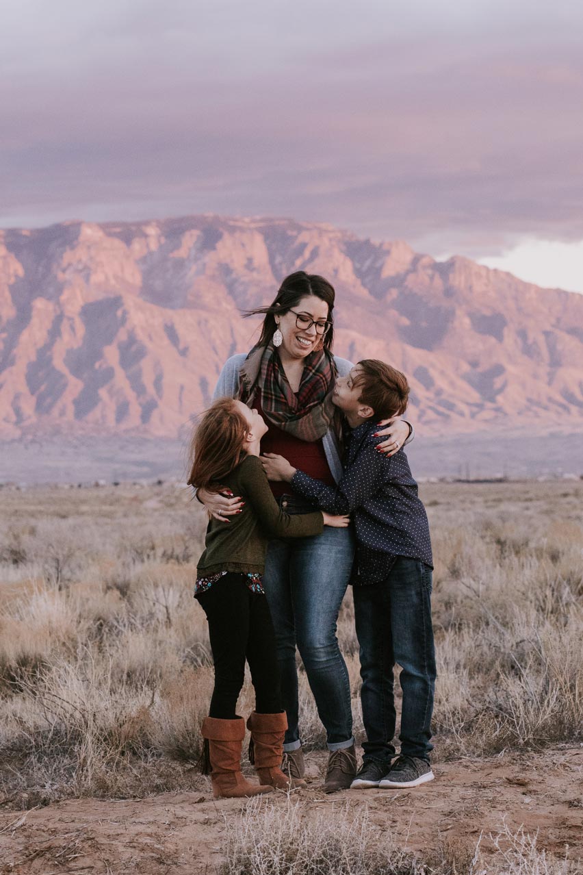 Smiling mom with son and daughter in front of sunset and Sandia mountains in Rio Rancho
