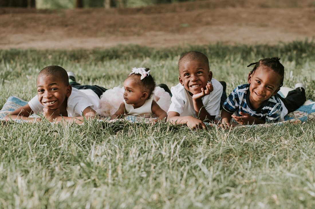 4 children lay on a blanket and smile at the camera.