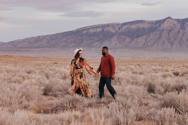 Couple hold hands and walk in front of the mountains.