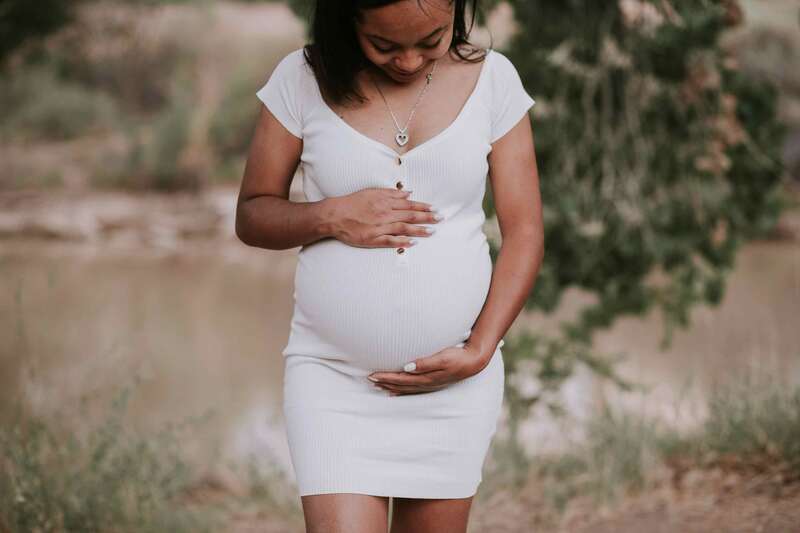 Pregnant mother in white dress looks down at belly.