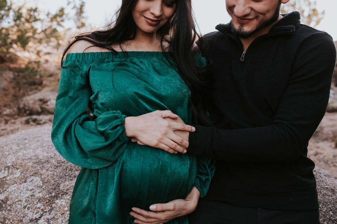 Couple smile and look down at pregnant mother's belly, while mom is dressed in green.