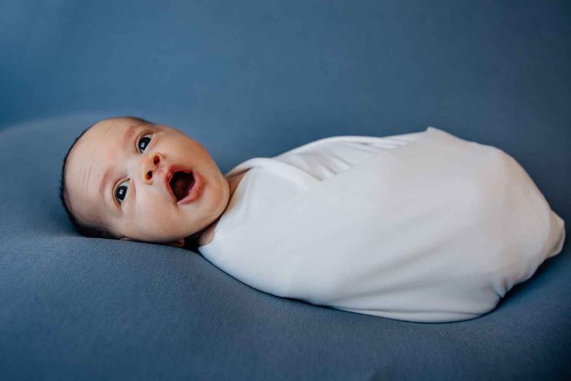Baby yawning wrapped in white on blue blanket.