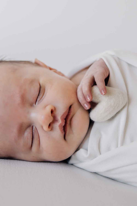 Newborn sleeping swaddled in white clutching small white heart