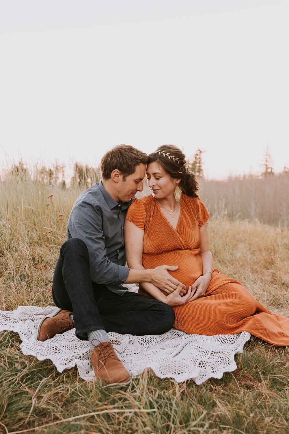 Pregnant woman sitting and snuggling with husband on blanket. She is in orange dress by your maternity photographer in Albuquerque