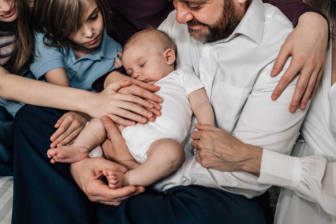 Family lay hands on baby and lean in and look at him.