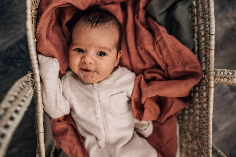Newborn smiling at camera on orange blanket in basket.