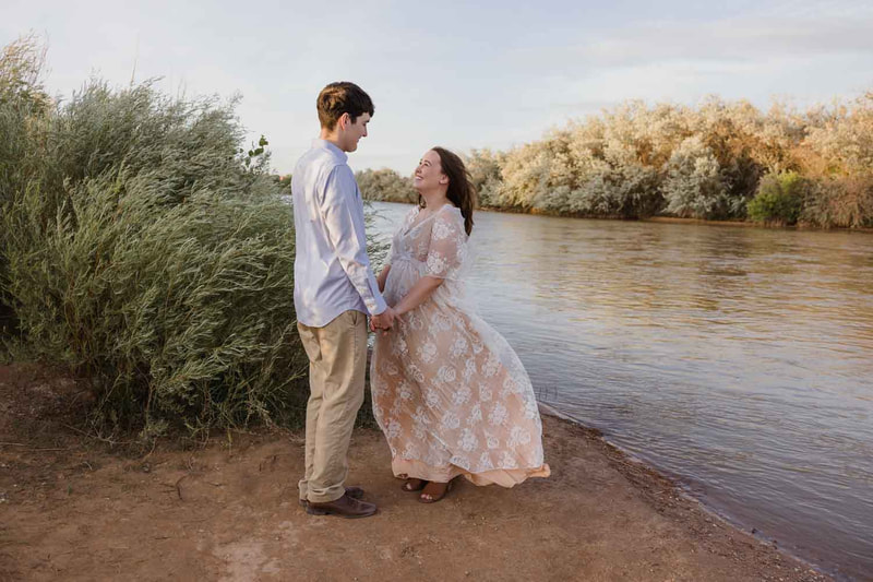 couple stands in front of river holding hands.