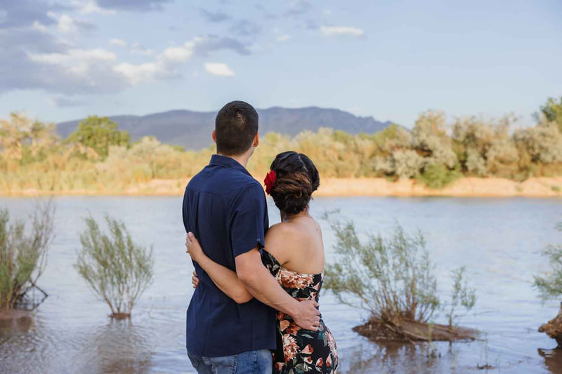 Couple snuggle together and look over the river to the mountain.