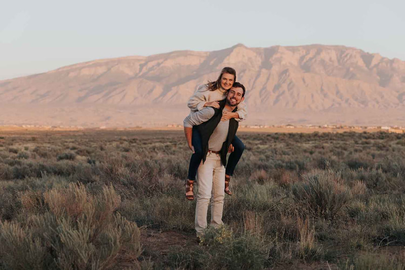 Man carries woman on his back in front of mountains.