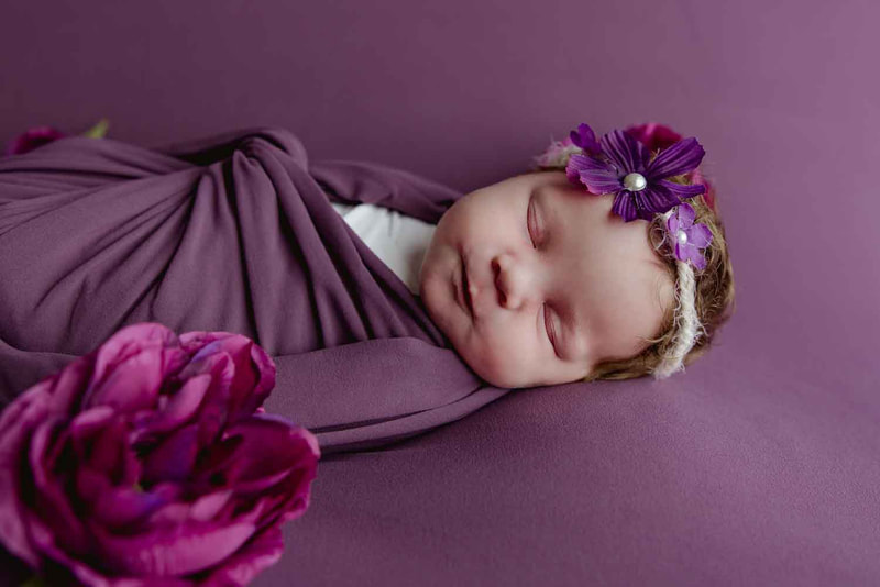 Baby girl wrapped in purple with purple flowers around her.