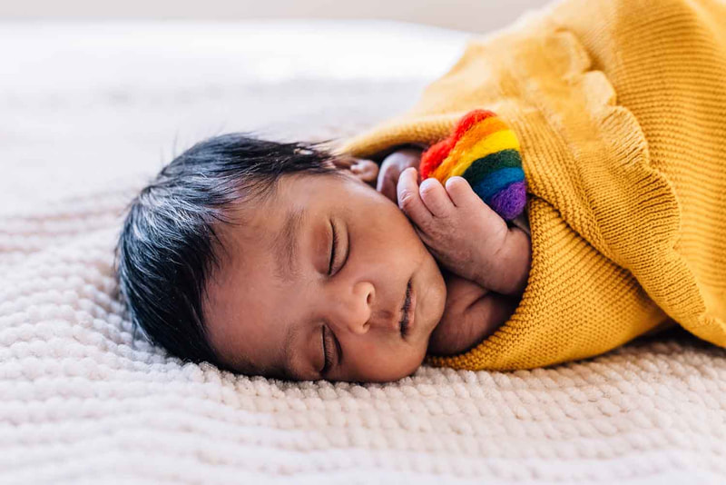 Baby swaddled in yellow holding rainbow heart.